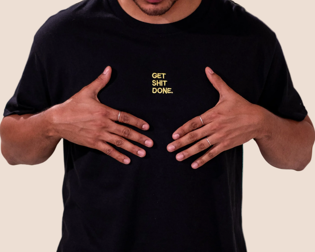 Person wearing a black t-shirt with 'GET SHIT DONE' text on a brown background