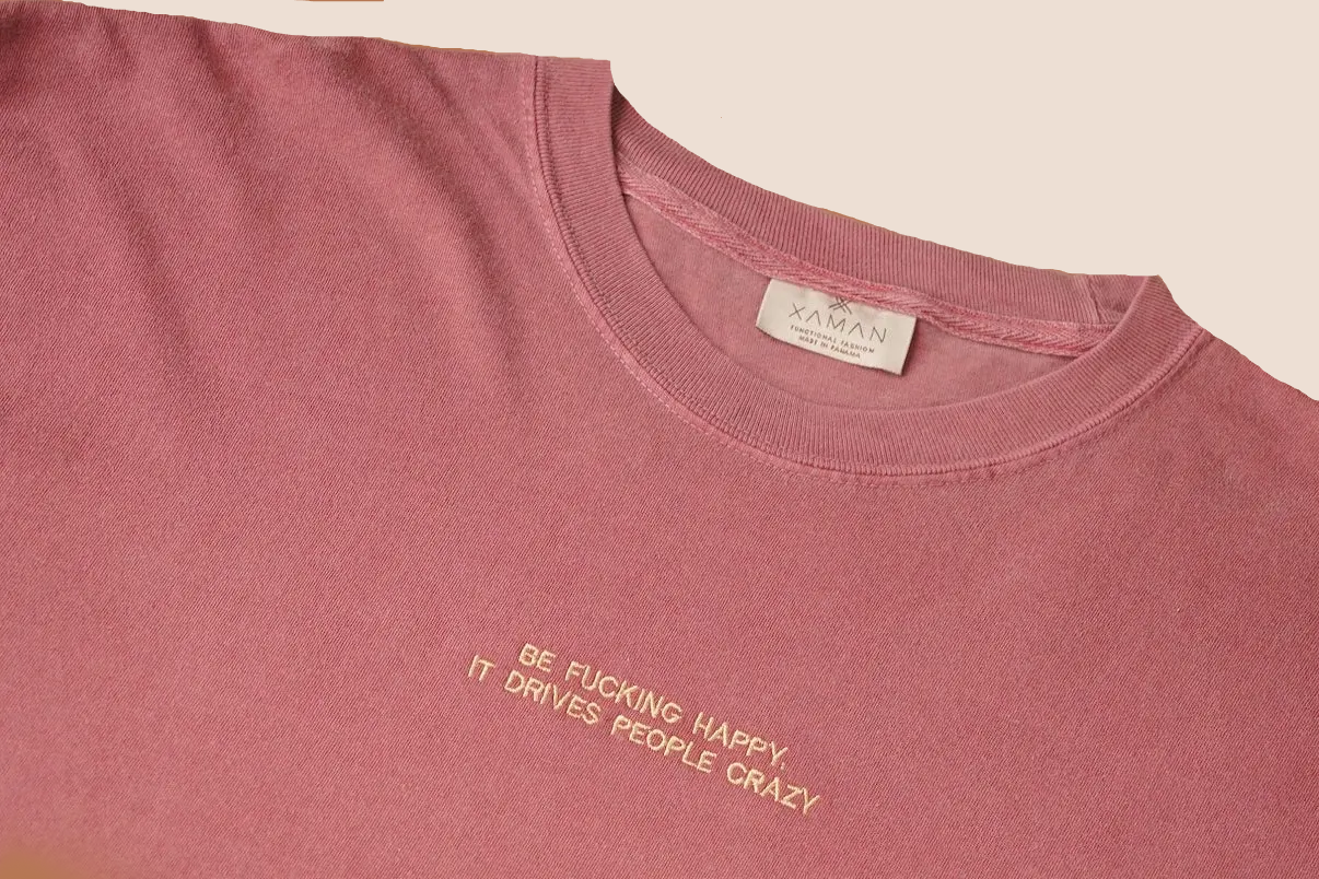 Pink t-shirt with text and a brand label on a brown background