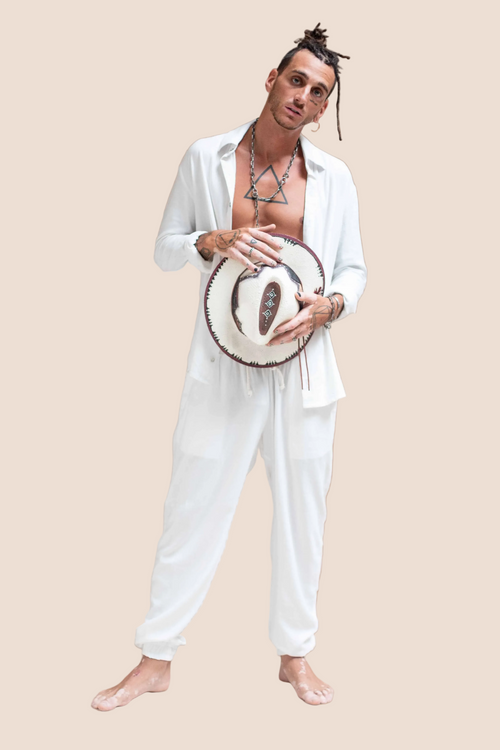 Man in white outfit holding a woven hat against a brown background