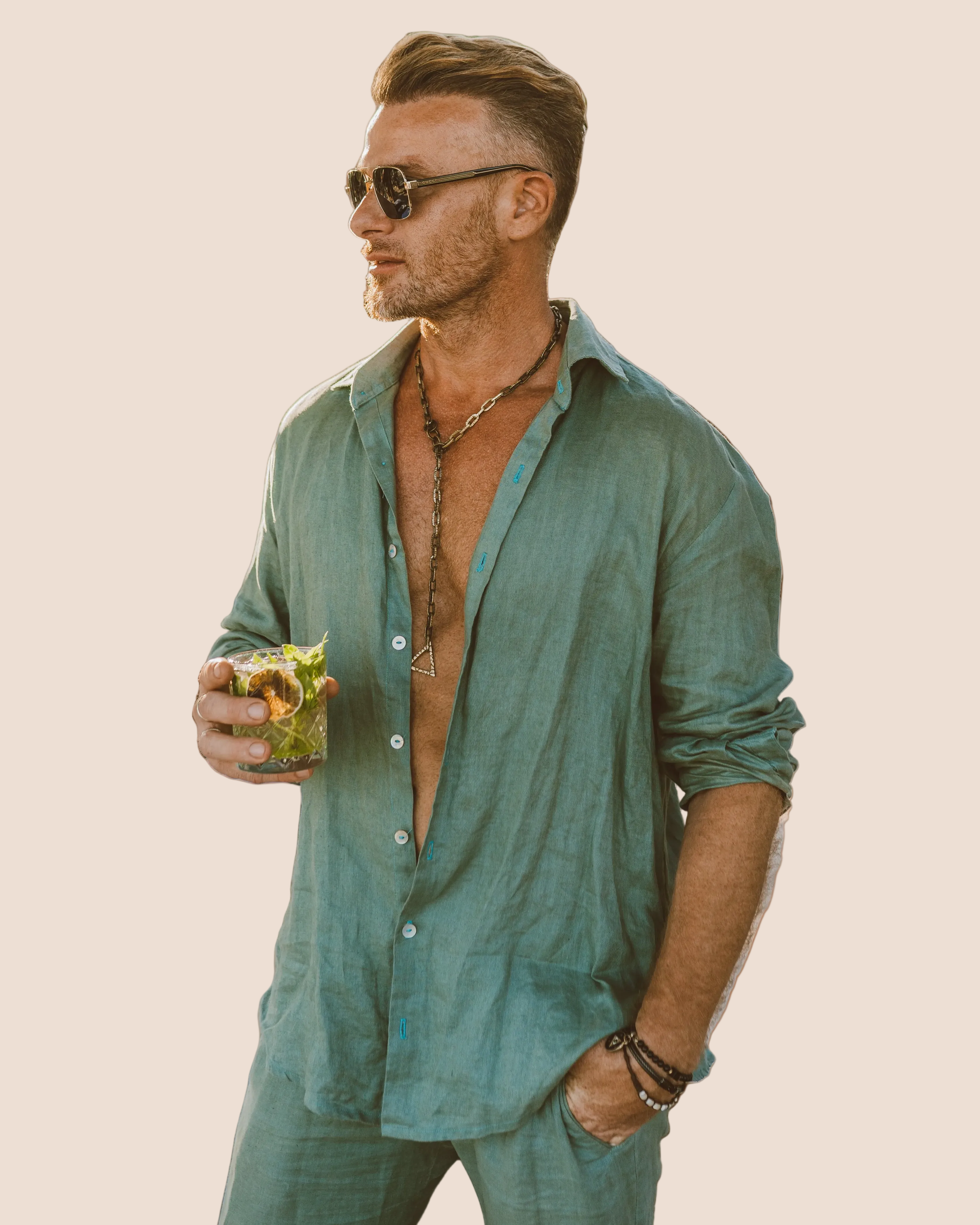 Man wearing a green shirt and sunglasses, holding a drink against a brown background
