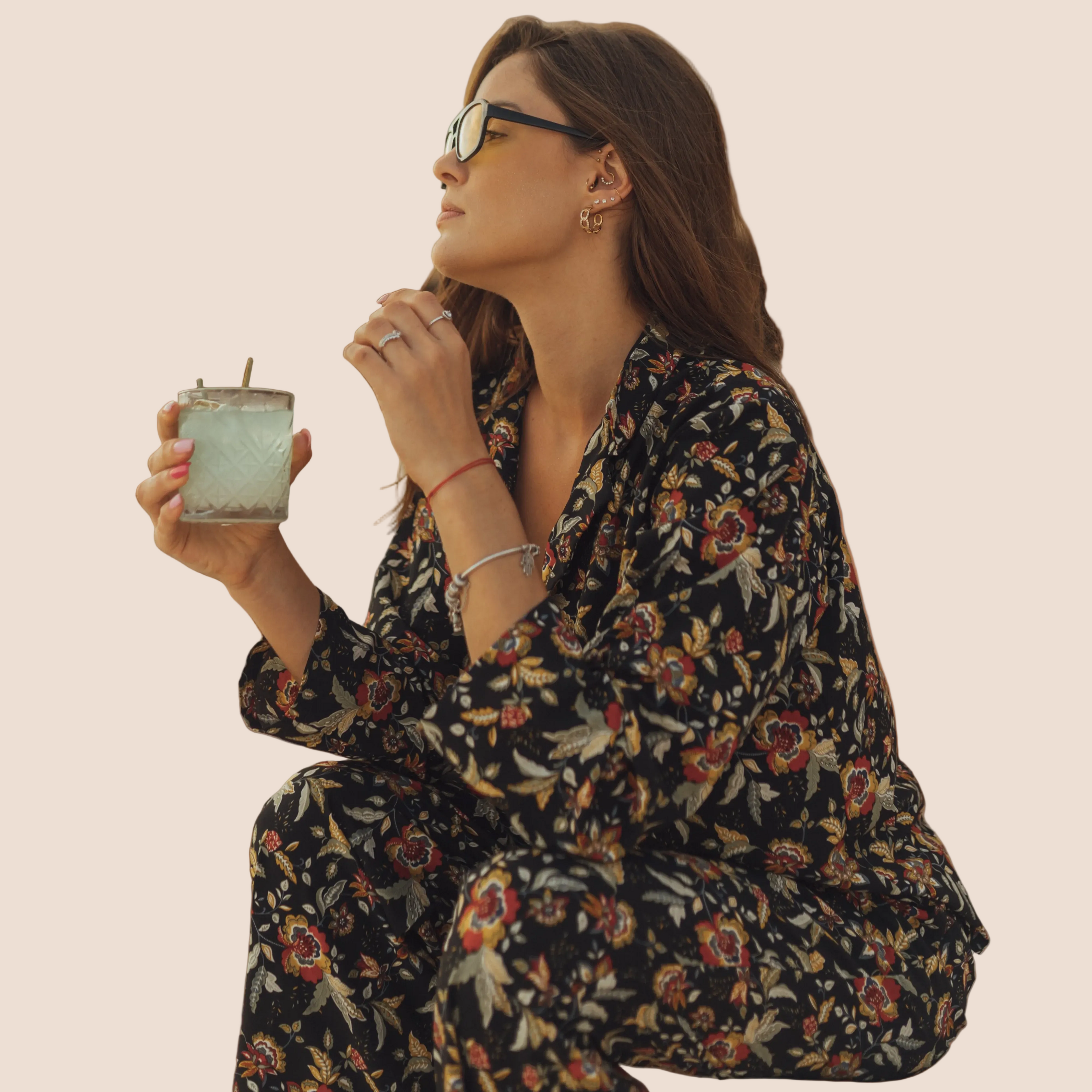 Woman in floral outfit holding a drink against a brown background