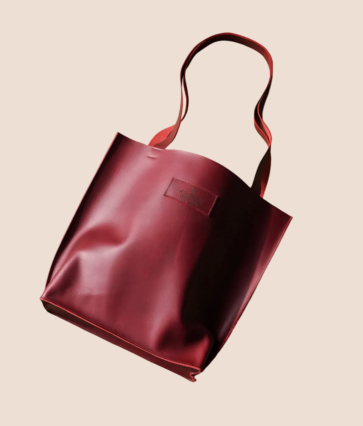 Maroon tote bag with a visible brand logo on a brown background
